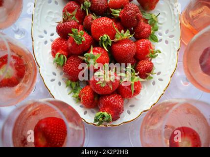Bicchieri da vino di rosa e deliziose fragole fresche su sfondo bianco, vista dall'alto Foto Stock