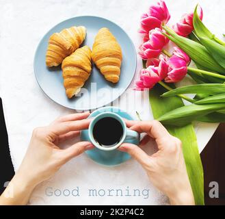 Ragazza con croissant e caffè, un bouquet di tulipani rosa, mattina felice Foto Stock