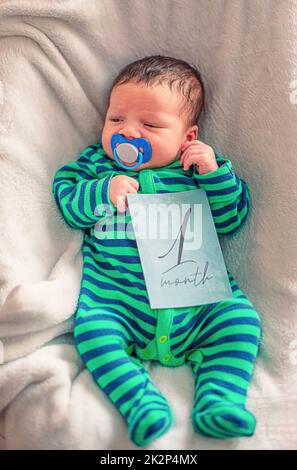 Bambino carino con la scheda di pietra miliare di 1 mesi nella sua mano Foto Stock