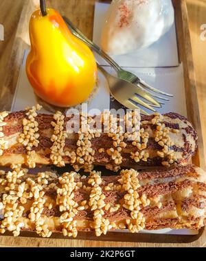Deliziose torte fresche, eclarie e dessert a forma di pera su un piatto di legno con forchette, dolciumi Foto Stock
