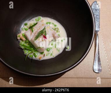 Merluzzo all'Alaska al vapore, piselli verdi, ebiko e limone in salsa di panna. Menu di portate principali nel raffinato ristorante servito al tavolo. Foto Stock