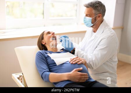 Dentista maschile trattamento denti di giovane donna incinta Foto Stock