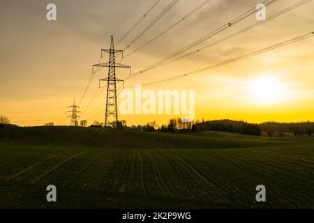 Polo elettrico ad alta tensione e linee elettriche di trasmissione al tramonto Foto Stock