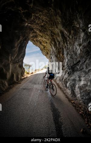 Strada maschile ciclista cavalcando attraverso un tunnel sulla strada balcone a Villard Notre Dame da Bourg d'Oisans, Alpi francesi. Foto Stock