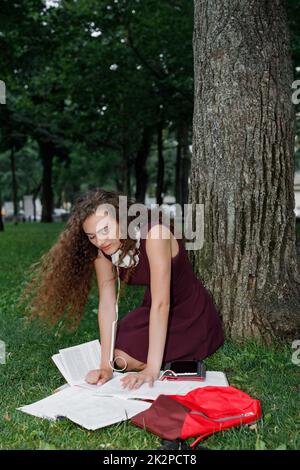 Una studentessa azienda prenota e seduto sotto agli alberi Foto Stock