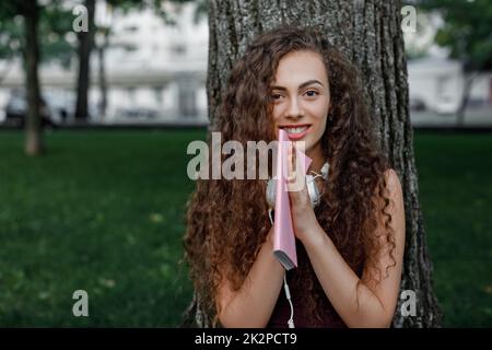 Una studentessa azienda prenota e seduto sotto agli alberi Foto Stock