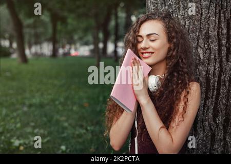 Una studentessa azienda prenota e seduto sotto agli alberi Foto Stock