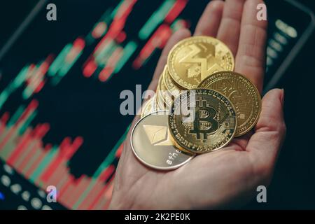 Mano che tiene varie monete di criptovaluta d'oro con grafico a bastone di candela e sfondo digitale Foto Stock