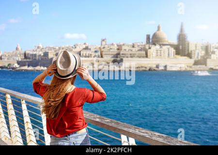 Turismo in Europa. Ragazza viaggiatore che tiene cappello a piedi lungo la passeggiata di Malta con la Valletta paesaggio urbano sullo sfondo. Foto Stock