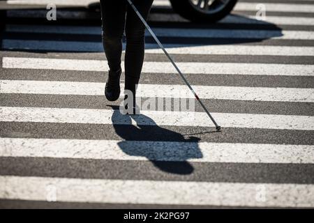 Donna cieca che cammina per le strade della città, utilizzando la sua canna bianca per navigare meglio lo spazio urbano e per raggiungere la sua destinazione in modo sicuro Foto Stock