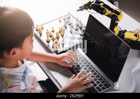 Codice di programmazione del bambino asiatico al braccio della macchina del robot sul laptop per giocare gli scacchi Foto Stock