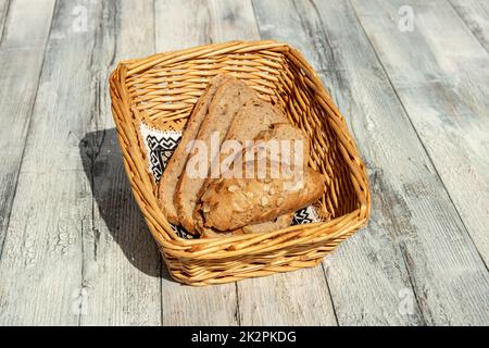 Primo piano di fette di pane fresco cotto intero in un cestino di vimini su un rustico tavolo di legno luminoso. Concetto di salute. All'aperto con luce naturale del sole. Foto Stock