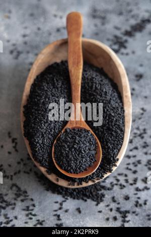 Spezie indiane cumino nero (nigella sativa o kalonji) semi in ciotola con cucchiaio su tavola di legno vista dall'alto. Foto Stock