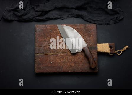 Tagliere in legno vuoto rettangolare e coltello da cucina su tavola nera con tovagliolo a garza, vista dall'alto Foto Stock