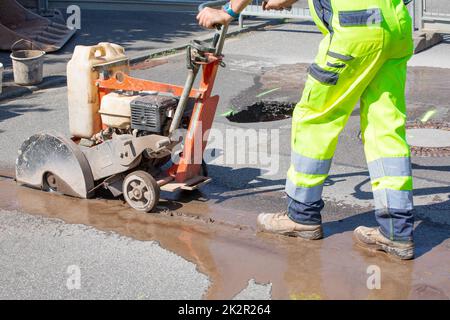 L'operatore stradale taglia il calcestruzzo con una macchina per il taglio del calcestruzzo Foto Stock