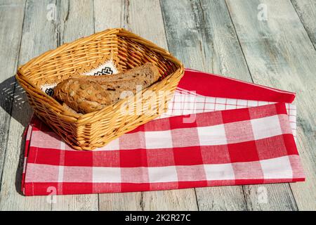 Primo piano di fette di pane fresco cotto a grani interi in un cestino di vimini su tovaglioli rossi con spazio su un tavolo rustico di legno luminoso. Concetto di salute. All'aperto con luce naturale del sole. Foto Stock