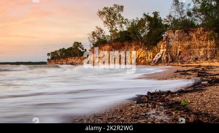 La vista a lunga esposizione delle onde marine che raggiungono la costa selvaggia con piante botaniche all'alba Foto Stock