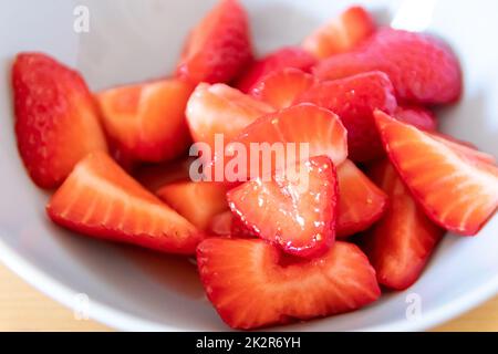 Molte fragole tagliate in ciotola sono pronte a mangiare con cucchiaio d'argento o come delizioso cibo per le dita e uno spuntino sano con frutta rossa e vitamine sul tavolo da cucina in legno per un'alimentazione e una salute sostenibili Foto Stock
