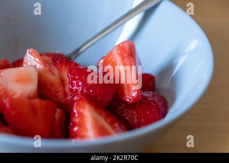 Molte fragole tagliate in ciotola sono pronte a mangiare con cucchiaio d'argento o come delizioso cibo per le dita e uno spuntino sano con frutta rossa e vitamine sul tavolo da cucina in legno per un'alimentazione e una salute sostenibili Foto Stock