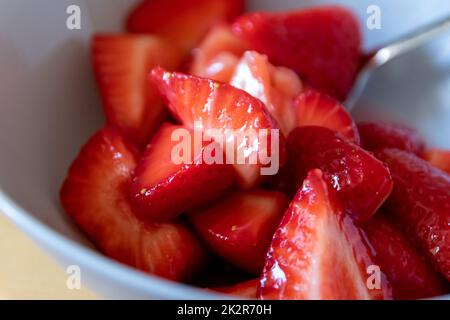 Molte fragole tagliate in ciotola sono pronte a mangiare con cucchiaio d'argento o come delizioso cibo per le dita e uno spuntino sano con frutta rossa e vitamine sul tavolo da cucina in legno per un'alimentazione e una salute sostenibili Foto Stock