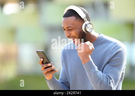 Uomo eccitato con pelle nera che controlla la musica sul telefono Foto Stock