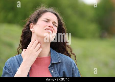 Donna sopraffatta che graffia il collo itchy in un parco Foto Stock