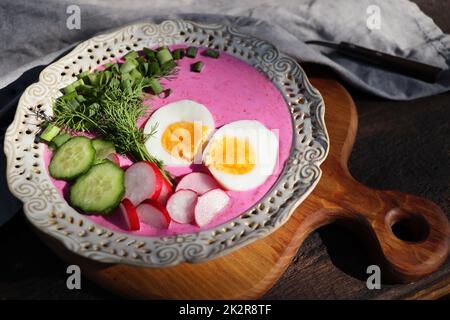 Zuppa fredda di barbabietole con uova, cetrioli, patate e verdure sul tavolo di legno. Specialità per le giornate calde. Profondità di campo poco profonda, messa a fuoco selettiva Foto Stock