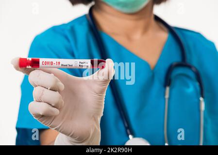 Infermiere in uniforme blu indossare una maschera che tiene il tubo di prova Prelevare un campione di sangue di analisi per il coronavirus Foto Stock