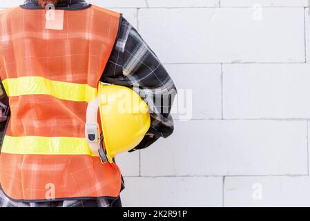 Vista posteriore di ingegnere, architetto, supervisore indossano indumenti riflettenti per la sicurezza dell'operazione di lavoro tenere casco di sicurezza Foto Stock
