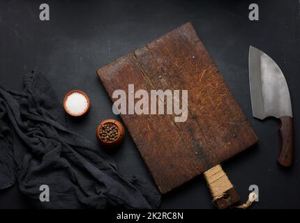 Tagliere in legno vuoto rettangolare e coltello da cucina su tavola nera con tovagliolo a garza, vista dall'alto Foto Stock