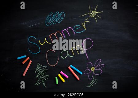Testo campo estivo scritto su lavagna nera, con bastoncini di gesso di diversi colori Foto Stock