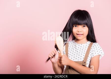 Bambino asiatico 10 anni tenere pettine spazzolarla unruly tocca i suoi lunghi capelli neri Foto Stock