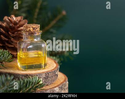 Bottiglia di vetro con olio essenziale di conifere vicino a rami di abete e coni di pino su primo piano verde Foto Stock