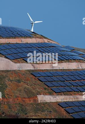 pannelli solari fotovoltaici e turbine eoliche che generano energia elettrica su colline e cielo blu. Ecologia verde natura concetto. Foto Stock