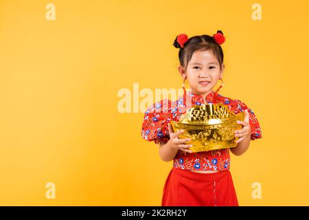 Felice ragazza cinese asiatica sorridere con gongsam rosso in possesso di grande lingotto d'oro Foto Stock