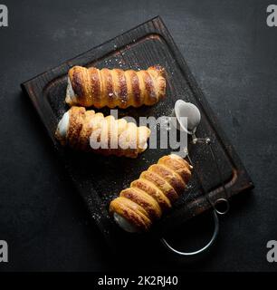 tubuli al forno riempiti con panna bianca montata su un tavolo da cucina in legno nero, vista dall'alto Foto Stock