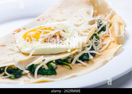 pancake farcito con foglie di spinaci servito con uova fritte e formaggio grattugiato Foto Stock