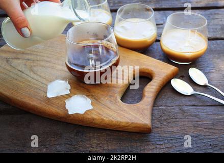 Le donne versano a mano la salsa di latte ghiacciata in un bicchiere di caffè. Rinfrescante drink estivo Foto Stock