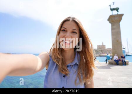 Primo piano della ragazza felice che prende autoritratto con la statua del cervo punto di riferimento della città di Rodi in Grecia Foto Stock