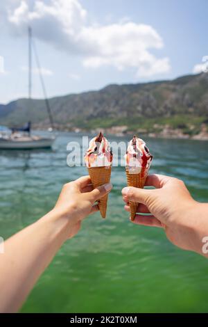 Molto bella passeggiata della baia di Cattaro, Montenegro. Coppia amatissima che tiene un gelato colorato sullo sfondo della baia di Cattaro. Foto Stock