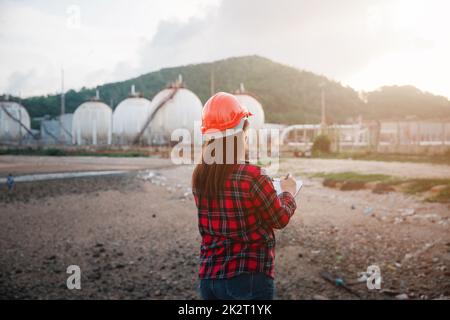 Donna operatrice asiatica felice nell'industria chimica del petrolio lavoratore di ispezione visiva elenco di lavoro sulla clipboard in pianta Foto Stock