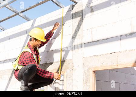 Addetto alle costruzioni o addetto alle costruzioni utilizzando il nastro di misurazione per il controllo dal telaio del tetto in acciaio alla portiera Foto Stock