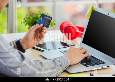 uomo d'affari che tiene la carta di credito e digita il codice di sicurezza su un computer portatile Foto Stock