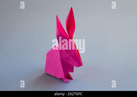 Origami di coniglio di carta rosa isolato su uno sfondo grigio Foto Stock
