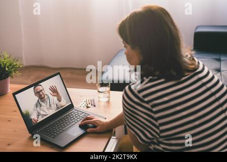 Donna seduta su un divano e parlare con un medico online utilizzando un computer portatile. Concetto di telemedicina. Foto Stock