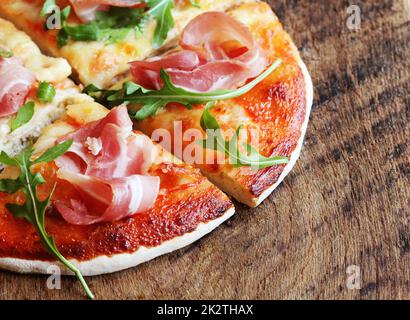 Pizza con prosciutto affumicato e Rucola su sfondo di legno Foto Stock