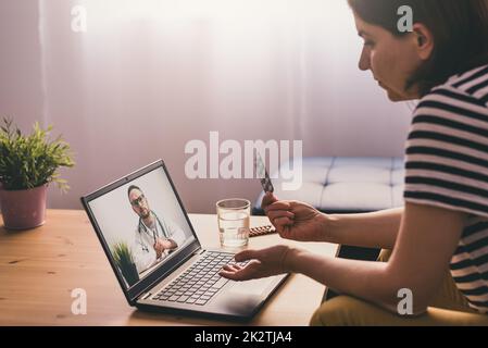 Donna seduta su un divano e parlare con un medico online utilizzando un computer portatile. Concetto di telemedicina. Foto Stock