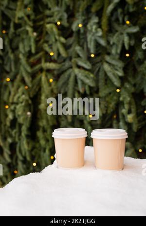 Due tazzine di caffè di carta all'aperto nella neve sullo sfondo di una bella parete verde nobilis, concetto di caffè da portare. Passeggiate all'aria aperta. Foto Stock