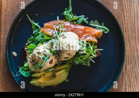 Uovo benedict con rucola, salmone e avocado su un piatto scuro nel ristorante per la prima colazione Foto Stock