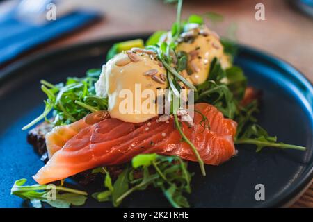 Uova Benedict con salmone e rucola su un piatto nero per la colazione nel ristorante. Messa a fuoco selettiva. Foto Stock